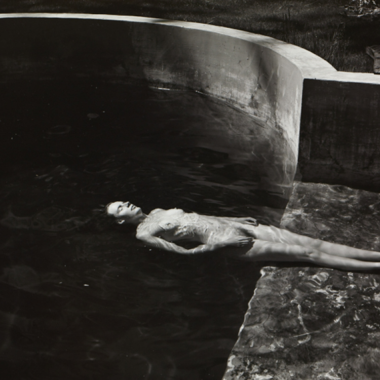 A black and white image of a naked woman floating in a pool