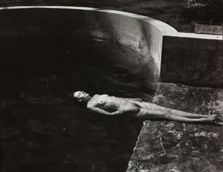 A black and white image of a naked woman floating in a pool