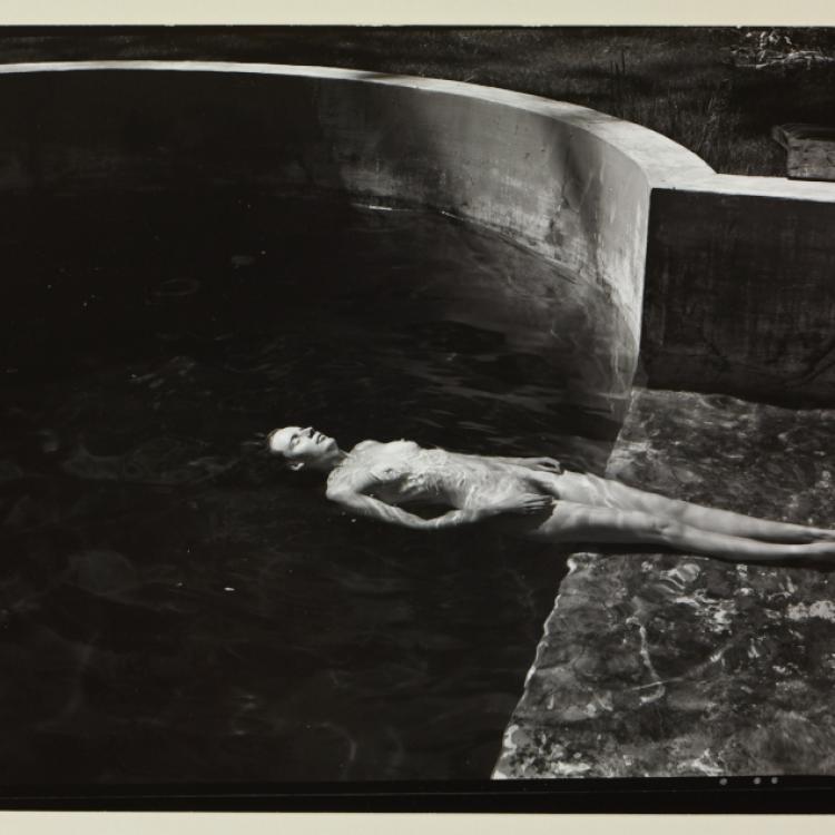 A black and white photograph of a nude woman facing up and floating in a pool