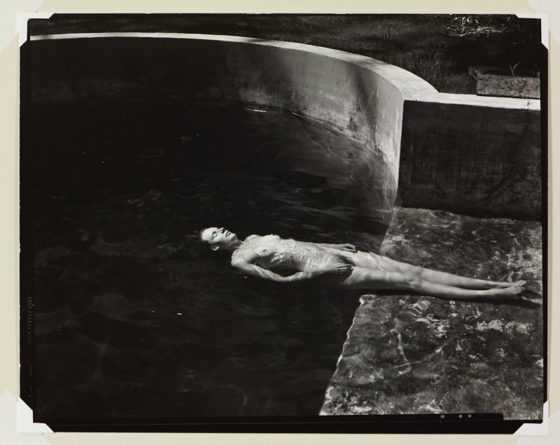 A black and white photograph of a nude woman facing up and floating in a pool