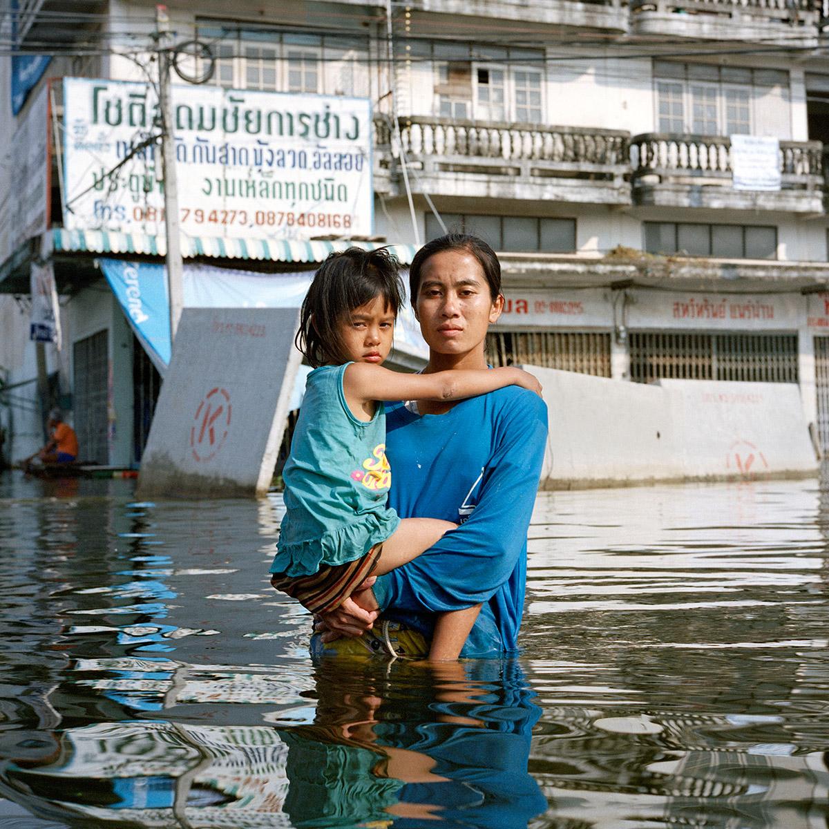 A woman carrying a child on a flooded street with water up to her waist